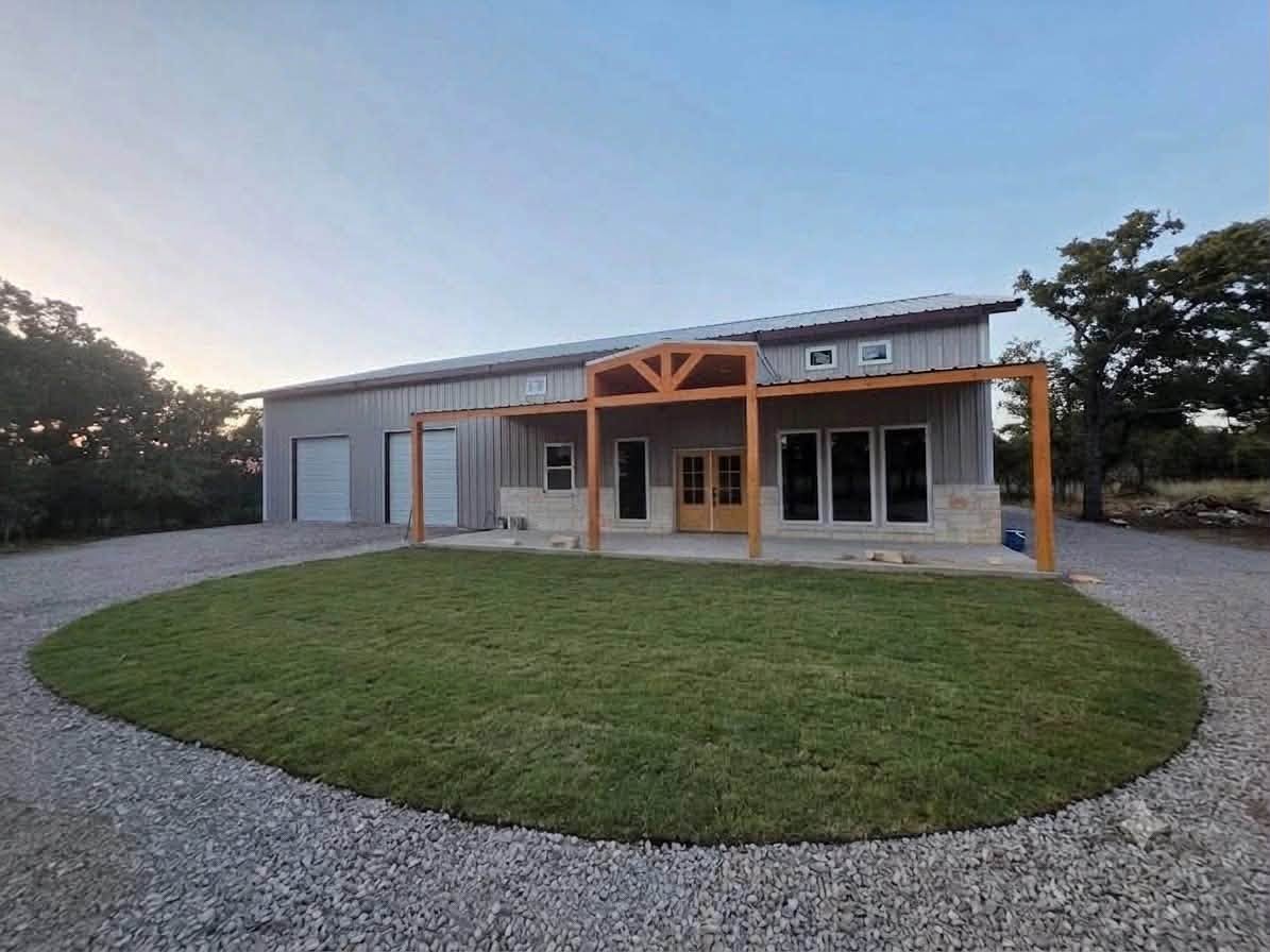 Metal-sided house with timber porch and stone accents, nearing completion